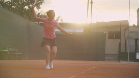 A-woman-playing-tennis-at-sunset-hits-a-flying-ball-on-a-tennis-court